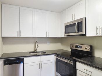A kitchen with white cabinets and black countertops at The Packard, West Hartford, Connecticut, 06119
